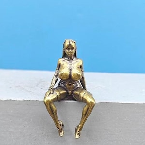 Puede incluir: Una figura de color bronce de una mujer sentada. La figura está detallada con una pose sentada, tacones altos y un atuendo sugerente. El fondo es de color azul claro sólido.