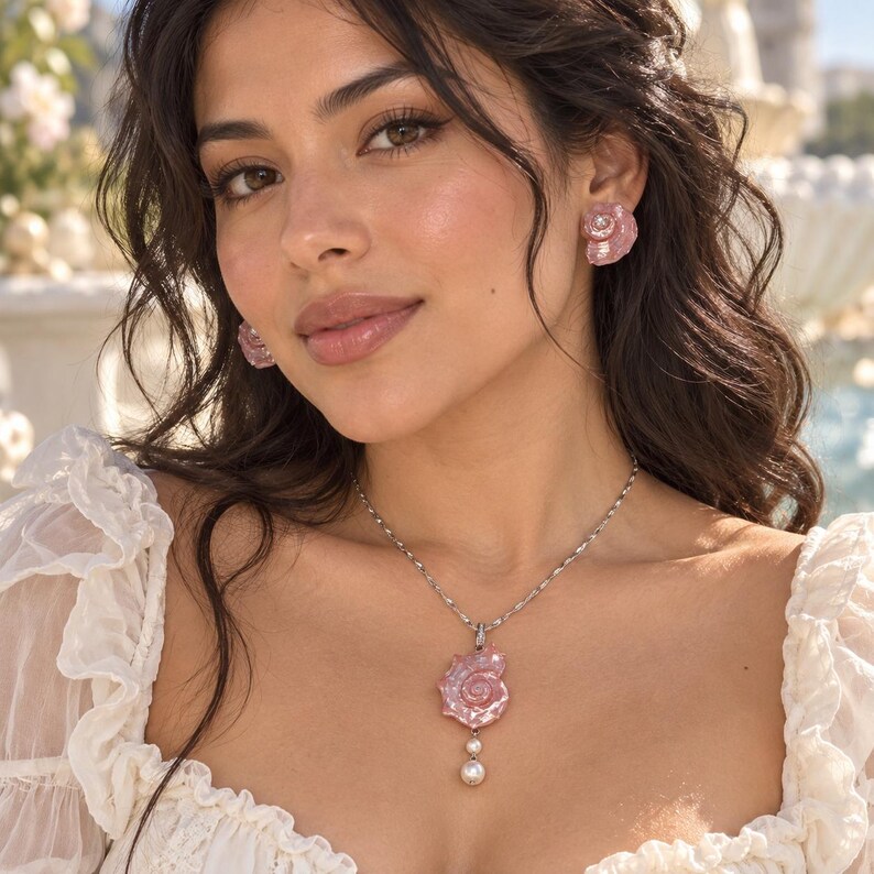 Puede incluir: Un conjunto de joyer&iacute;a que consiste en un collar de cadena plateada con un colgante de concha marina rosa y una perla blanca colgante, junto con pendientes de bot&oacute;n a juego en forma de concha rosa. El collar presenta una cadena de eslabones.