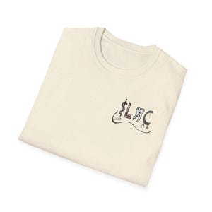 May include: Cream-colored t-shirt with a crew neck. The shirt features a small graphic on the front, including the letters "LAC", a caduceus, a tooth, a stethoscope, and the year "2025". The graphic is in black and red.