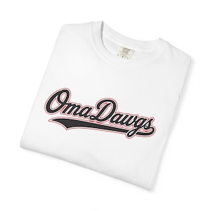 Könnte beinhalten: Ein weißes kurzärmeliges T-Shirt mit dem Schriftzug Oma Dawgs in schwarzer Schreibschrift, umrandet von einer roten Linie und einem schwarzen Unterstrich. Das Comfort Colors Markenetikett am Innenkragen zeigt die Größe L an.
