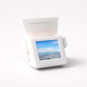May include: A white, miniature, retro-style television with a small screen displaying a scenic ocean view under a blue sky. The TV has a hinged top and side details, suggesting a vintage aesthetic. The overall design is clean and minimalist.