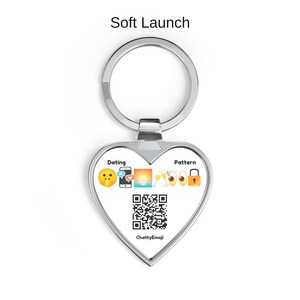 Puede incluir: Un llavero de plata en forma de coraz&oacute;n con el texto Soft Launch en la parte superior. El centro muestra las palabras Dating y Pattern flanqueando una fila de emojis que incluyen una cara pidiendo silencio, smartphone, atardecer.