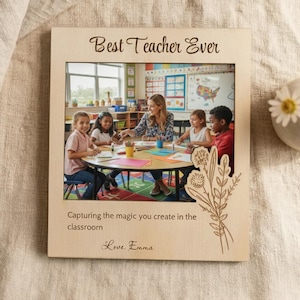 Op de afbeelding: Houten fotolijst met de tekst "Best Teacher Ever" en een foto van een leraar met leerlingen. De lijst bevat de tekst "Capturing the magic you create in the classroom" en "Love, Emma". Een bloemenontwerp is op het frame geëtst.