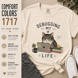 Op de afbeelding: Crèmekleurig T-shirt met een afbeelding van een kat met een bril, werkend op een laptop. De tekst luidt "Debugging My Life". Extra tekst is "this error makes no sense". Het shirt is ontworpen voor kattenliefhebbers en heeft een vintage look.