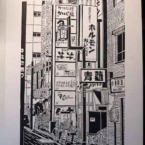 May include: Black and white linocut print depicting a street scene in Shinjuku, Japan. The artwork features numerous signs with Japanese text, storefronts, and architectural details. The print is titled "Signs of Shinjuku".