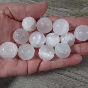May include: A collection of white selenite spheres, also known as satin spar, in various sizes. The spheres are smooth and polished, with a translucent, milky white appearance.