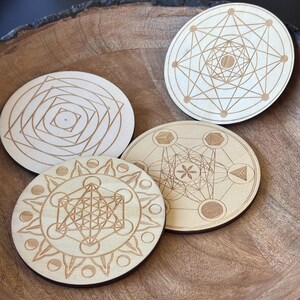 May include: Four round wooden coasters with geometric designs. Each coaster features a different etched pattern, including interconnected lines, circles, and shapes. The coasters are light brown in color and appear to be made of natural wood.