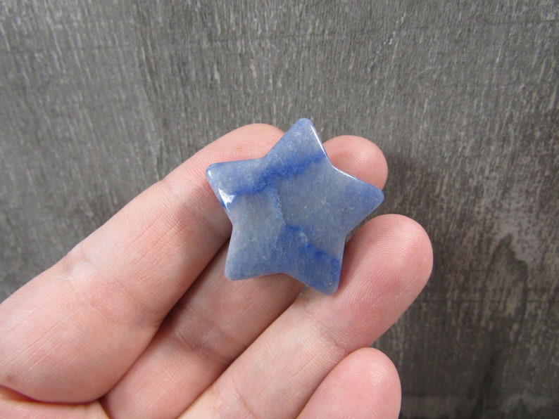 blue quartz star 26 mm shaped crystal displayed on fingers with grey wooden background