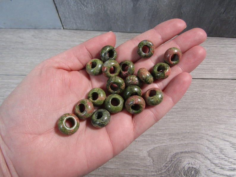 unakite 14 mm pi stone donut bead displayed in an open hand with a wooden grey background