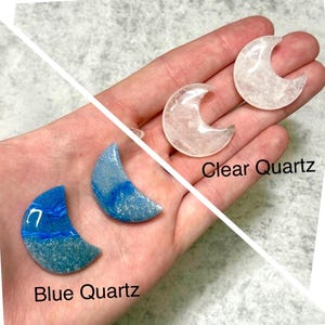 May include: A hand displays three crescent moon-shaped crystals. Two are clear quartz, and two are blue quartz. The blue quartz has a marbled appearance. The text "Clear Quartz" and "Blue Quartz" are visible.
