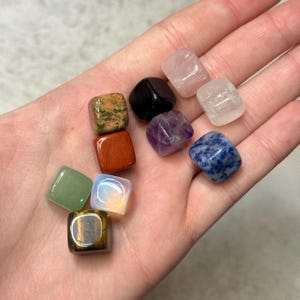 Puede incluir: Una colección de gemas cuadradas y coloridas en varios colores, incluyendo verde, rojo, morado y azul. Las gemas se sostienen en una mano, mostrando sus superficies pulidas y patrones únicos. Las gemas son una mezcla de diferentes tipos.