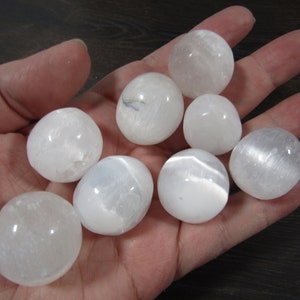 White selenite medium tumbled stones in a hand with black background