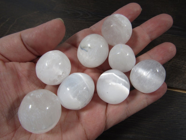 White selenite medium tumbled stones in a hand with black background