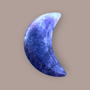May include: A crescent-shaped, polished stone in shades of blue and purple. The gemstone has a smooth, glossy surface with a marbled appearance. The object is set against a neutral background.