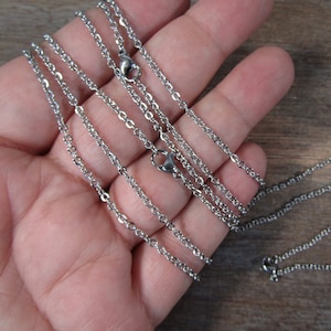 May include: A set of four silver chain necklaces of varying lengths. The chains are made of a thin, delicate metal and have a simple, classic design.