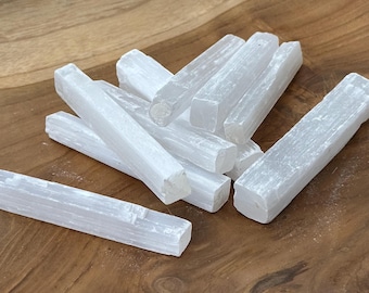 May include: A collection of white selenite crystal wands, each with a rectangular shape and a smooth, translucent appearance. The wands are arranged on a wooden surface, showcasing their natural texture and subtle variations in color.