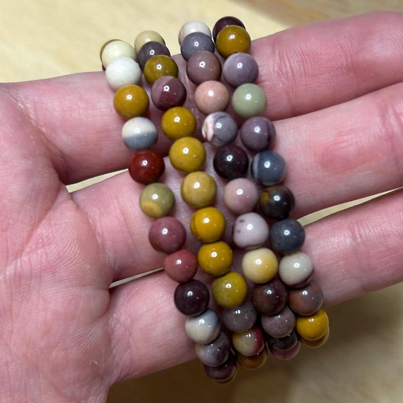 May include: Four beaded bracelets with a variety of colors including yellow, red, purple, and gray. The bracelets are made of small, round beads and are stacked together. The beads have a polished finish and are strung on an elastic cord.