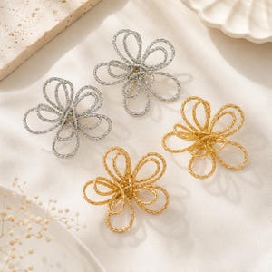 May include: Four flower-shaped earrings featuring a textured, wire-like design. Two earrings are finished in a bright silver tone, and two earrings are finished in a warm gold tone. Each piece consists of multiple overlapping loops forming petals.