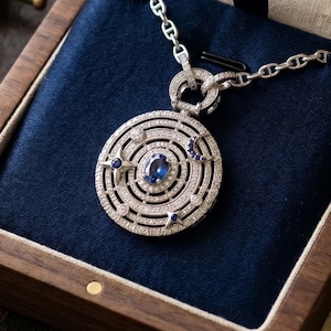 May include: A silver pendant necklace with a celestial design, featuring a large oval blue gemstone at the center. The pendant is adorned with small white gemstones and blue star and crescent moon accents. The necklace is displayed in a wooden box with a blue velvet lining.