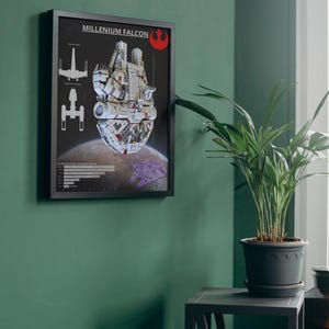 Puede incluir: Póster enmarcado con el Halcón Milenario, una nave espacial de Star Wars, con esquemas y un fondo planetario. El póster tiene un marco negro y está montado en una pared verde. Se ve un símbolo rojo de la Alianza Rebelde.