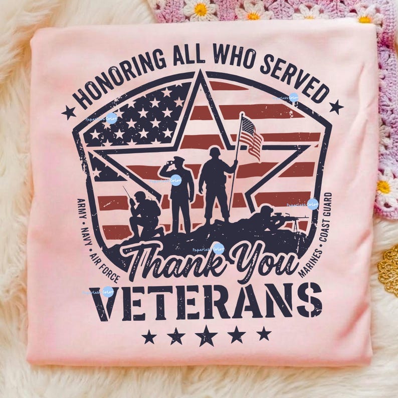 Puede incluir: Una camiseta rosa claro con un dise&ntilde;o patri&oacute;tico. El dise&ntilde;o incluye un emblema en forma de estrella con la bandera estadounidense, siluetas de soldados y el texto "HONORING ALL WHO SERVED" y "Thank You VETERANS".
