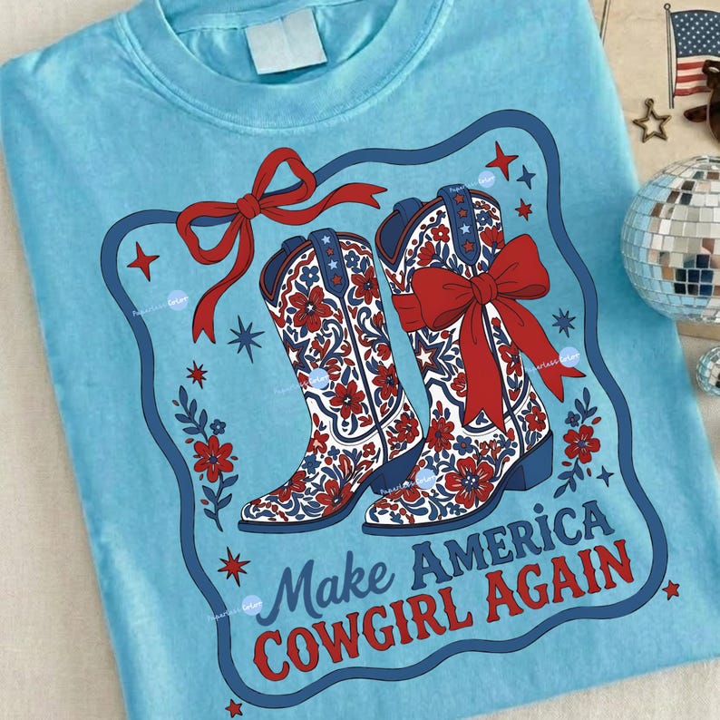 Puede incluir: Camiseta azul claro con un dise&ntilde;o de dos botas de vaquero con lazos rojos y estampados florales. Las botas est&aacute;n enmarcadas en azul y rojo, con el texto "Make America Cowgirl Again" debajo.