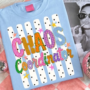 May include: A light blue t-shirt featuring a graphic print of white vertical stripes with black polka dots. The text "CHAOS Coordinator" is displayed in large, colorful, patterned letters, accented by small pink, orange, and yellow star shapes.