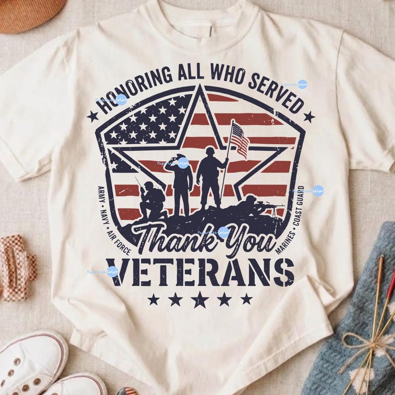 Puede incluir: Camiseta color crema con un dise&ntilde;o patri&oacute;tico. El gr&aacute;fico incluye un emblema en forma de estrella con la bandera estadounidense, siluetas de soldados y el texto "Honoring All Who Served" y "Thank You Veterans".