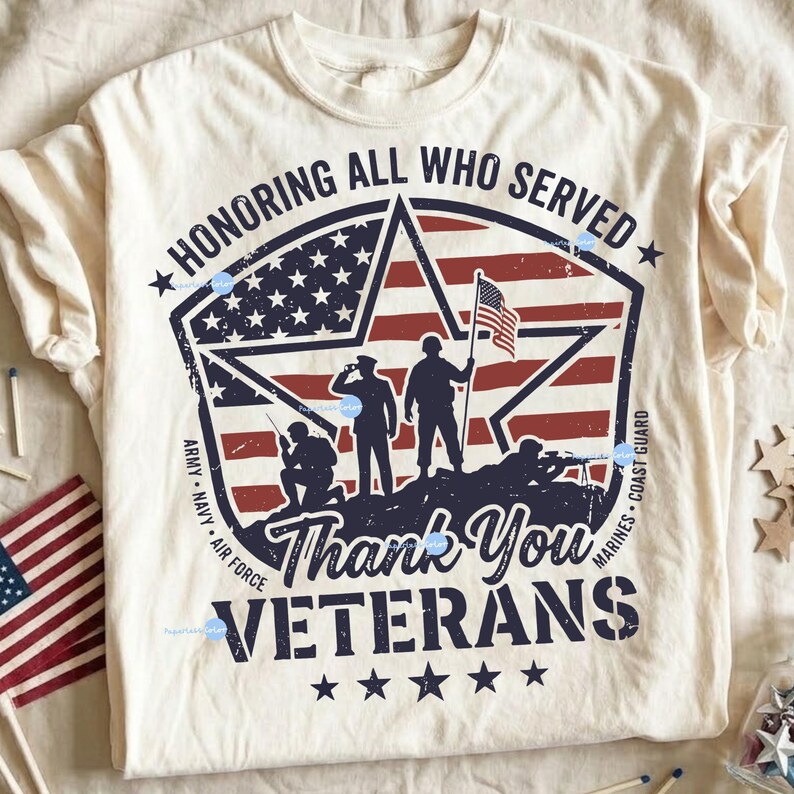 Puede incluir: Camiseta de color crema con un dise&ntilde;o patri&oacute;tico. El gr&aacute;fico incluye un emblema en forma de estrella con la bandera estadounidense, siluetas de soldados y el texto "Honoring All Who Served" y "Thank You Veterans".