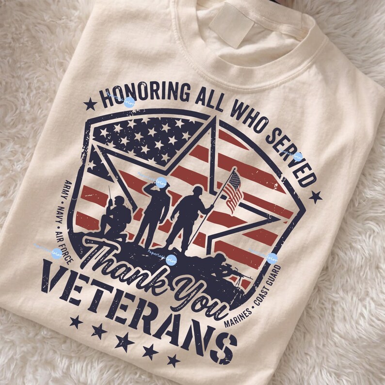 Puede incluir: Camiseta de color crema con un dise&ntilde;o patri&oacute;tico. El gr&aacute;fico incluye un emblema en forma de estrella con la bandera estadounidense, siluetas de soldados y el texto "Honoring All Who Served" y "Thank You Veterans".