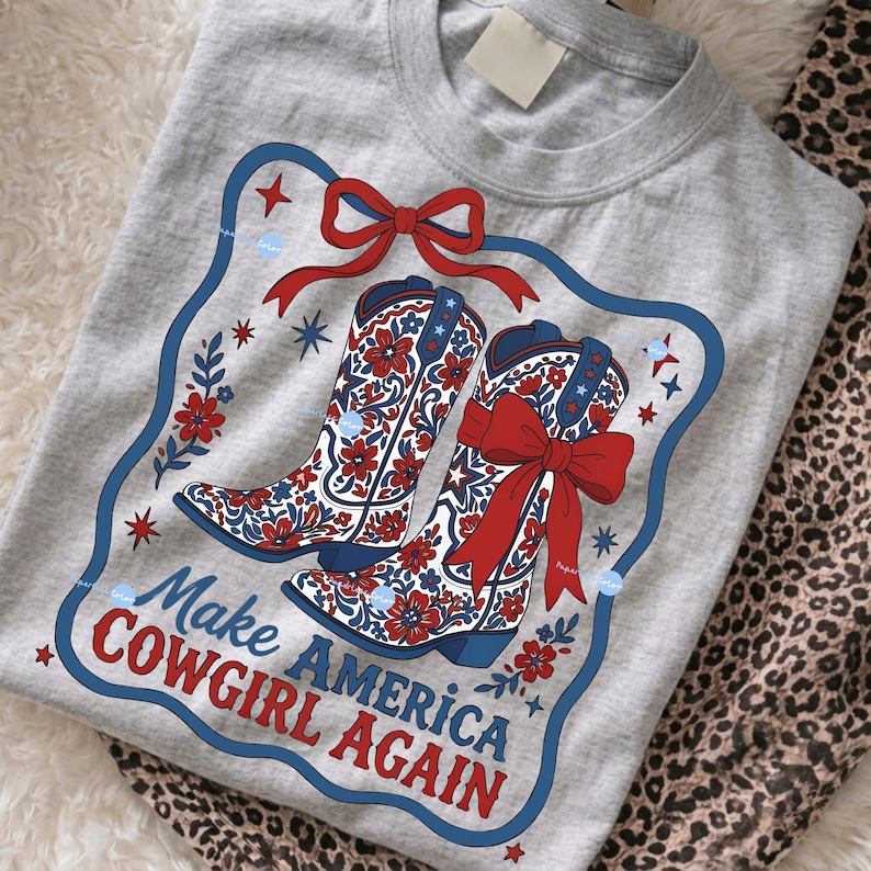 Puede incluir: Camiseta gris con un dise&ntilde;o de dos botas de vaquero con lazos rojos y motivos florales. Las botas est&aacute;n enmarcadas en azul y rojo, con el texto "Make AMERICA COWGIRL AGAIN".