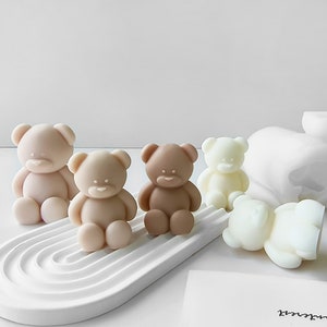 Könnte beinhalten: Fünf kleine Teddybär-förmige Seifen in verschiedenen Farben. Die Seifen sind auf einer weißen, gekrümmten Oberfläche angeordnet. Die Seifen sind beige, braun und weiß.
