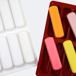 Peut inclure: Deux moules à glace en silicone. L'un est blanc et vide, l'autre est rouge et rempli de glaces colorées orange, rose et jaune. Les moules sont conçus pour créer des friandises glacées de forme rectangulaire.