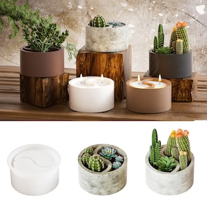 May include: Two concrete candle holders with a yin yang design. The candles are white and brown. The holders are surrounded by small potted plants.