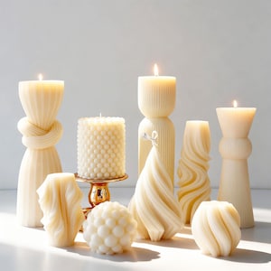 Könnte beinhalten: Eine Sammlung cremefarbener Wachskerzen in verschiedenen skulpturalen Formen, darunter geknotete, gerippte, kugelförmige und gedrehte Designs. Mehrere Kerzen brennen und strahlen ein sanftes Licht aus. Eine Kerze steht auf einem kleinen, goldenen Podest.