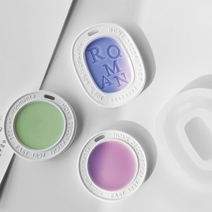 Può includere: Tre stampi rotondi in silicone bianco per realizzare diffusori di profumo. Gli stampi hanno un bordo rialzato e un foro nella parte superiore per l'appeso. Gli stampi sono riempiti con cere di diversi colori. Il testo sugli stampi recita "HOME DECORATION" e "EAST 1897".