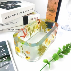 以下が含まれることがあります： 縁が高く透明な長方形の樹脂製のトレイで、押し花と葉が敷き詰められています。トレイは、黄色、オレンジ、赤、緑の押し花と葉で飾られています。