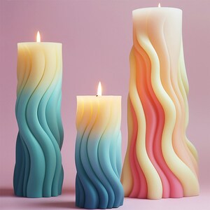 K&ouml;nnte beinhalten: Drei bunte Kerzen mit einem wellenf&ouml;rmigen Design. Die Kerzen sind in verschiedenen Gr&ouml;&szlig;en und brennen. Die gr&ouml;&szlig;te Kerze ist rosa und gelb, die mittlere Kerze ist blau und gelb und die kleinste Kerze ist blau und gelb.