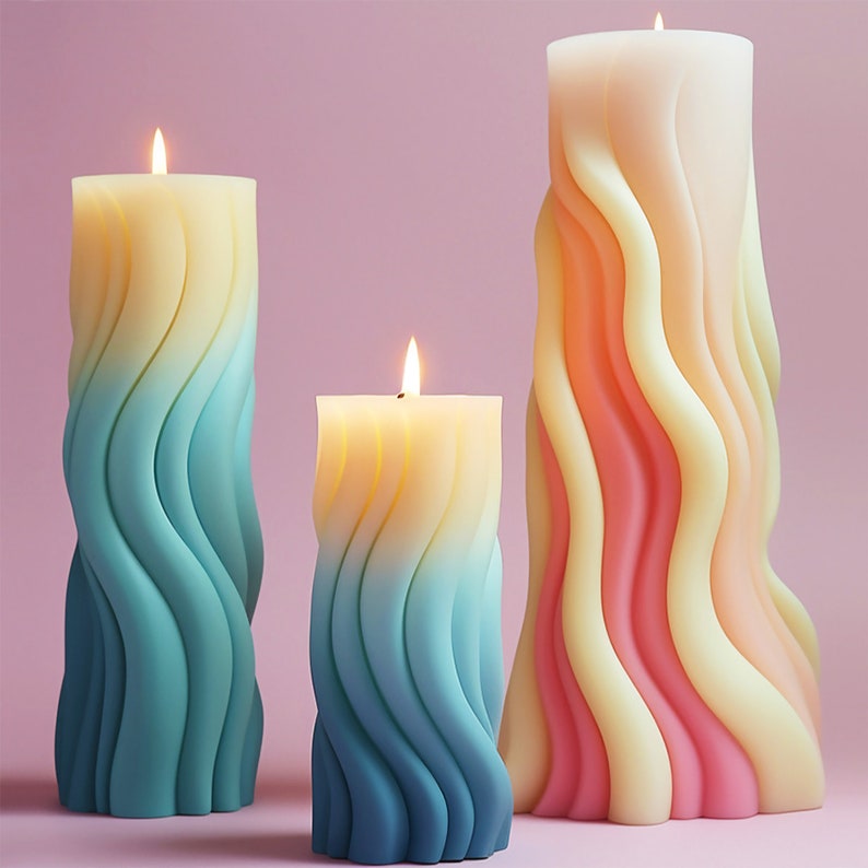 K&ouml;nnte beinhalten: Drei bunte Kerzen mit einem wellenf&ouml;rmigen Design. Die Kerzen sind in verschiedenen Gr&ouml;&szlig;en und brennen. Die gr&ouml;&szlig;te Kerze ist rosa und gelb, die mittlere Kerze ist blau und gelb und die kleinste Kerze ist blau und gelb.