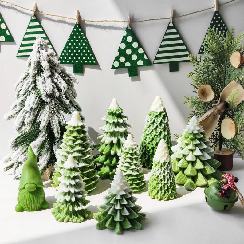 May include: A collection of green and white Christmas tree decorations, including a gnome, a bell, and a variety of small, frosted trees. The trees are arranged on a white surface with a string of green and white Christmas tree ornaments hanging in the background.