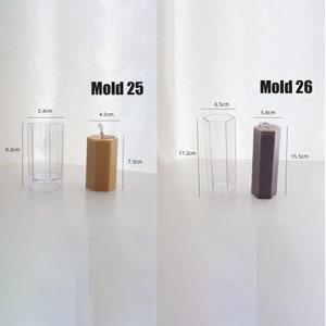 May include: Two hexagonal candle molds with measurements in centimeters. The mold on the left is clear plastic and the mold on the right is gray. The mold on the left has a yellow candle inside and the mold on the right has a dark gray candle inside. The text "Mold 25" is above the left mold and the text "Mold 26" is above the right mold.