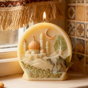 May include: A cream-colored candle with a detailed relief of a mosque, camel, and crescent moon. The candle has a lit wick and is placed on a windowsill. The design includes a mosque with domes and minarets, a camel, and a tree.