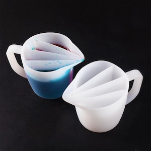 Könnte beinhalten: Zwei weiße Silikon-Messbecher mit einem geteilten Ausguss. Die Becher haben drei Abschnitte zum Abmessen verschiedener Flüssigkeiten. Ein Becher ist mit blauer und violetter Flüssigkeit gefüllt.