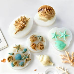 Könnte beinhalten: Eine Sammlung von Muschelförmigen Formen in verschiedenen Größen und Designs. Die Formen sind mit farbigem Harz gefüllt, darunter Brauntöne, Blau und Grün. Das Bild zeigt eine Vielzahl von Bastelbedarf zum Thema Meer, ideal für DIY-Projekte.
