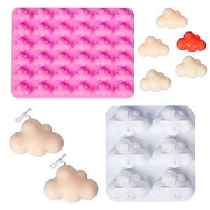 Puede incluir: Una colección de artículos con forma de nube. Un molde de silicona rosa está lleno de formas de nube. Se muestran varias velas con forma de nube en crema y rojo. Un molde de silicona blanco contiene formas de nube. También se muestran dos velas de nube de color crema con mechas.