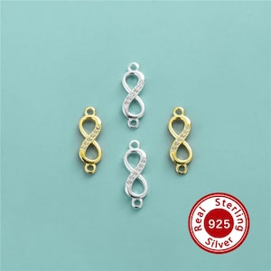May include: Four infinity symbol jewellery connectors arranged in a diamond pattern. Two are gold-toned and two are silver-toned, each featuring a row of small clear stones along one side and a small loop at the top and bottom. A red circular seal reads Real Sterling Silver 925.
