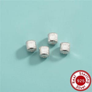May include: Four square-shaped silver beads with a textured, ribbed surface pattern. Each bead features a central hole for stringing. A circular red stamp in the corner displays the text Real Sterling 925 Silver.