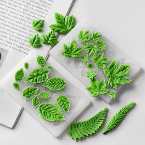 Puede incluir: Moldes de silicona verdes con forma de hoja para manualidades. La imagen muestra varios diseños de hojas, incluyendo hojas de arce y helecho, en diferentes tamaños. Ideales para crear elementos decorativos.