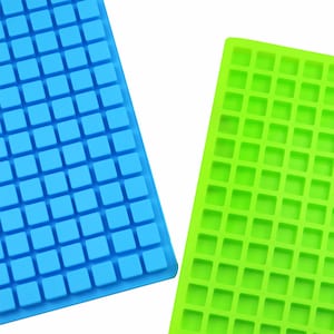 Puede incluir: Se muestran dos moldes de silicona, uno azul y otro verde. Cada molde es rectangular y presenta una cuadrícula de pequeñas cavidades cuadradas. Es probable que los moldes se utilicen para hacer cubitos de hielo, bombones u otras pequeñas delicias.