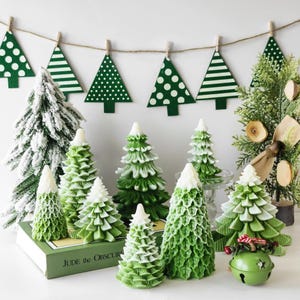 May include: A collection of green and white Christmas tree candles, some with a frosted finish, arranged on a table with a book titled "Jude the Obscure".